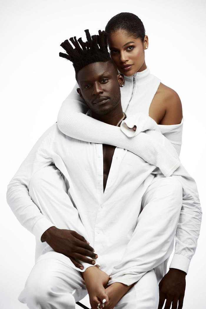 A stylish portrait of a couple in white clothing, embracing with a minimalist background.